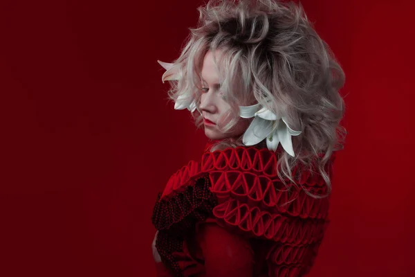 Tonos de rojo. Extraña mujer atractiva en un traje rojo, sobre un fondo rojo, con flores de lirio en el pelo . —  Fotos de Stock