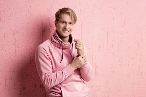 Friendly blond student guy in pink hoodie on pink background, copy space. — Stock Photo, Image