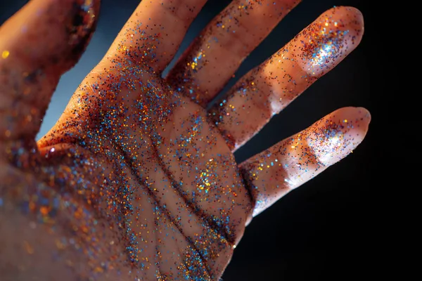 Weibliche Hand mit Pailletten bedeckt. die Bewegung der Handfläche und Glanz bunten Glitzers, — Stockfoto