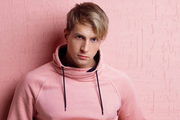Fiatal férfi rózsaszín kapucnis pulcsiban, rózsaszín háttérrel, — Stock Fotó