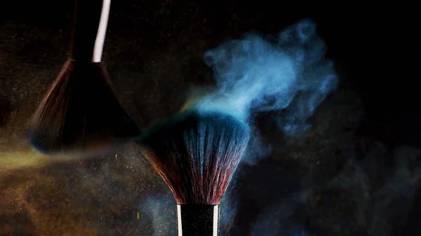 Twee zachte cosmetische borstels vrijgeven een wolk van gekleurde rook uit heldere oogschaduw en poeder, — Stockfoto