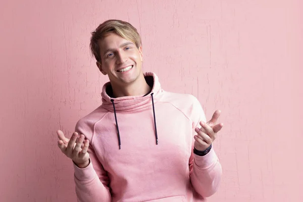 Young man in a pink hoodie on a pink background, happy and smiling — Stock Photo, Image