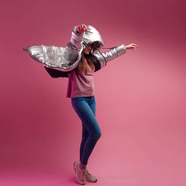 Fashionable and modern young woman in a puffy light down jacket throws a hood over her head. — Stock Photo, Image