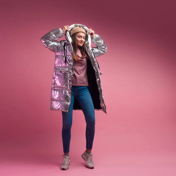 Modieuze en moderne jonge vrouw in een gezwollen licht donsjas gooit een kap over haar hoofd. — Stockfoto