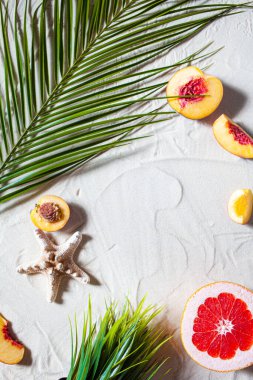 Plaj tatili Bir palmiye yaprağı, denizyıldızı ve beyaz ağaç dalı ve sulu meyveler beyaz kum üzerinde uzanır. Masaüstü duvar kağıdı.