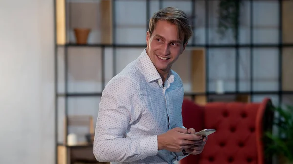 Smiling young man in white shirt, portrait in loft interior, stylish room.