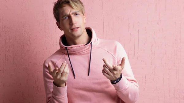 Young man in a pink hoodie thinks about the problem, a portrait of a guy on a pink background — Stock Photo, Image