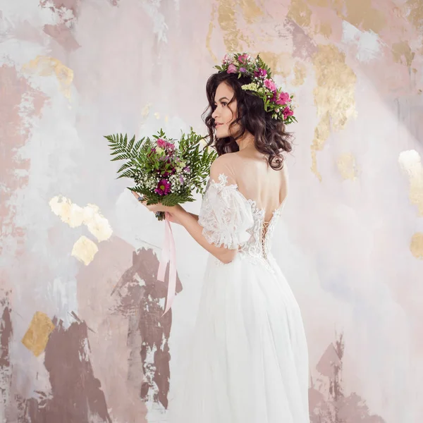 Elegante brunette meisje bruid met bloemen. Mooie jonge bruid in een weelderige bruiloft krans van verse bloemen — Stockfoto