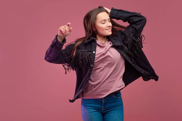 Glad flicka i en frans jacka danser på en rosa bakgrund. — Stockfoto