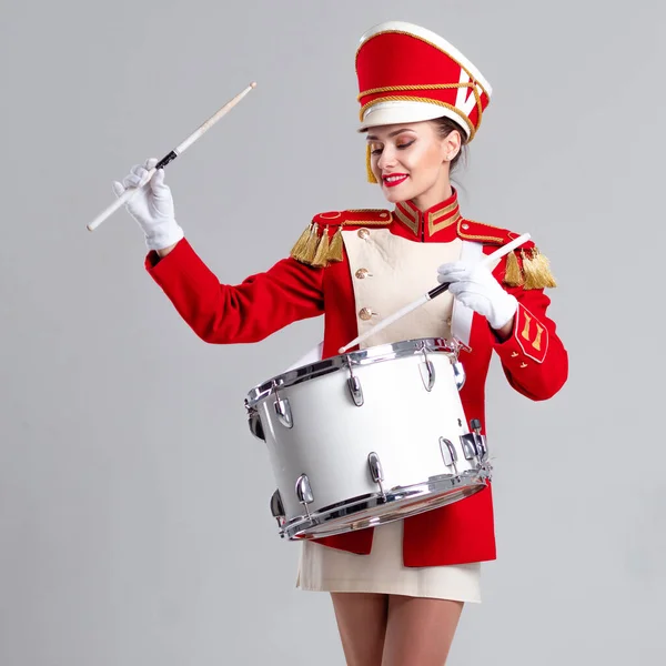 cheerful young woman in a red cap and uniform plays a drum.