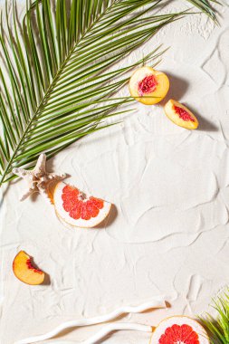 Plaj tatili Bir palmiye yaprağı, denizyıldızı ve beyaz ağaç dalı ve sulu meyveler beyaz kum üzerinde uzanır. Masaüstü duvar kağıdı.