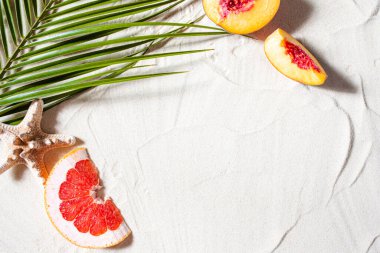 Sahil tatili. Bir palmiye yaprağı ve sulu meyveler beyaz ince kum üzerinde yatıyor. Masaüstü duvar kağıdı.