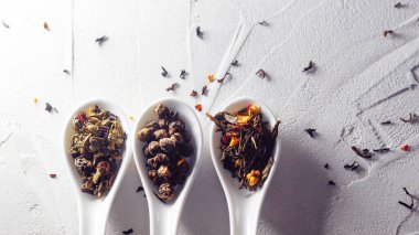 Beyaz desenli arka planda çay yapraklarının farklı çeşitleri kaşıkları ölçer. Çay demlemeye.