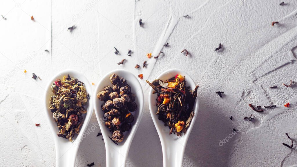 Different varieties of tea leaves in white measuring spoons on a white textured background. To brew tea