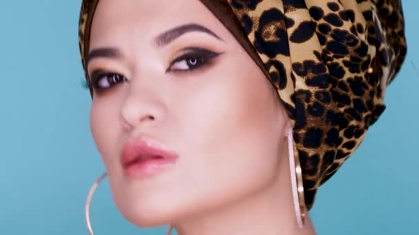 En attraktiv ung kvinna i en snygg turban tillverkad av leopardmönster tyg på en blå bakgrund. — Stockvideo