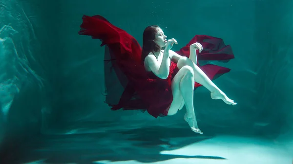 赤いドレスの美しい少女が水中で泳いでいます。水中では — ストック写真