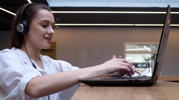 Étudiante utilise un ordinateur portable et Internet pour la formation. Une jeune femme dans un casque — Video