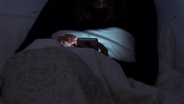 Молодая женщина в постели по ночам пользуется смартфоном. Социальные сети и прокрутка в Интернете , — стоковое видео