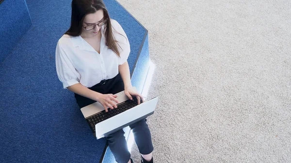 Joven estudiante utiliza un ordenador portátil. Una joven morena se sienta y escribe en un teclado , — Foto de Stock