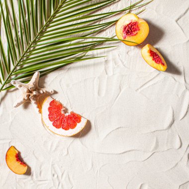 Plaj tatili Bir palmiye yaprağı, denizyıldızı ve beyaz ağaç dalı ve sulu meyveler beyaz kum üzerinde uzanır. Masaüstü duvar kağıdı.