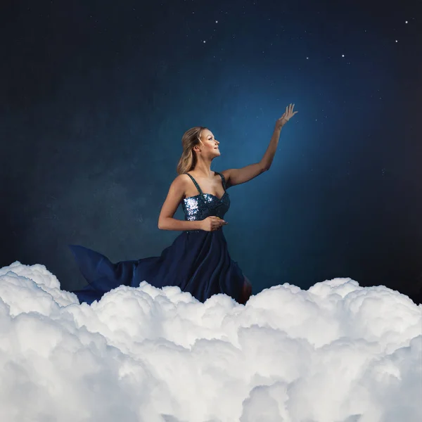 Romantique jeune femme en robe bleue contre un ciel bleu tire sa main vers le haut . — Photo