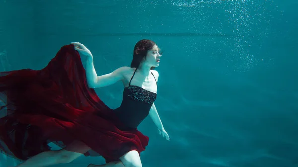 Schöne Mädchen in einem roten Kleid schwimmt unter Wasser. Erstaunliche Unterwasserwelt — Stockfoto