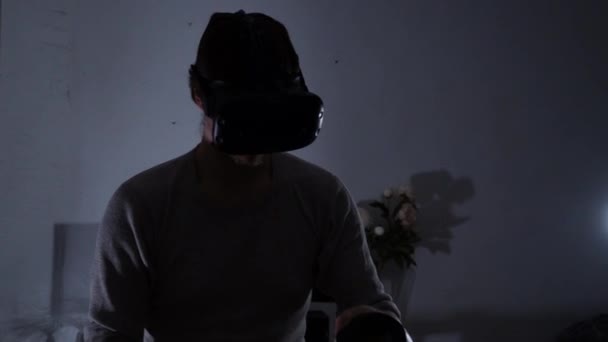 Young man at night or in the evening wearing a virtual reality helmet uses controllers — Stock Video