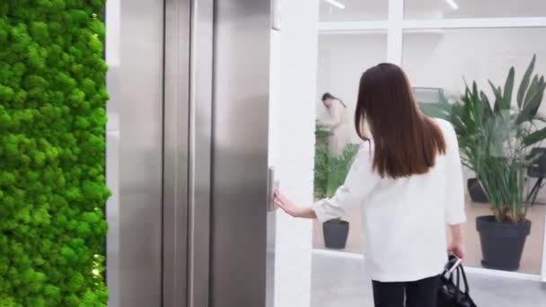 Charmante jonge zakenvrouw belt de lift in de lobby van het business center. — Stockvideo