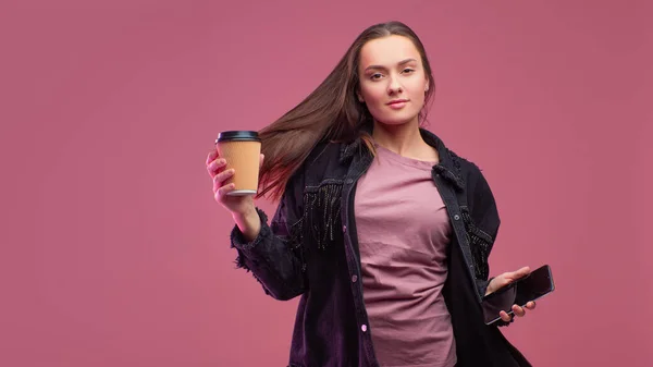 Joven estudiante con una taza de café de cartón y un teléfono inteligente en sus manos . — Foto de Stock