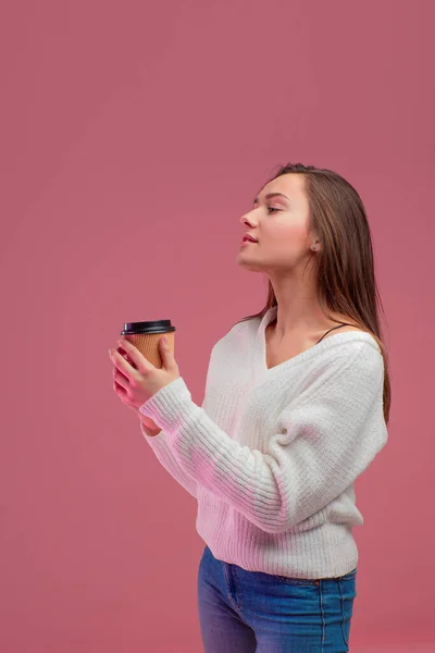 Encantadora joven morena en un suéter y jeans sostiene un vaso desechable para una bebida caliente , — Foto de Stock
