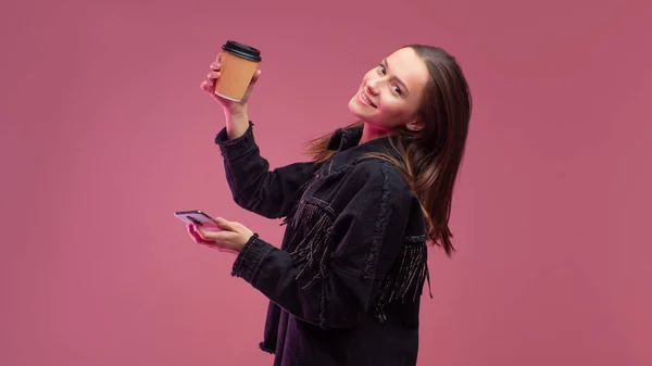 Jonge student met een kartonnen koffiebeker en een smartphone in haar handen. — Stockfoto