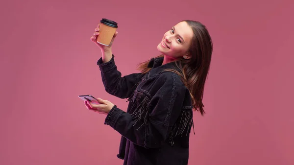 Junge Studentin mit einer Kaffeetasse aus Pappe und einem Smartphone in der Hand. — Stockfoto