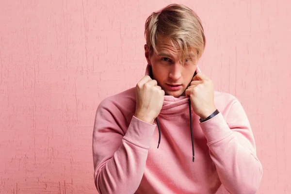 Friendly blond student guy in pink hoodie on pink background, copy space. — Stock Photo, Image