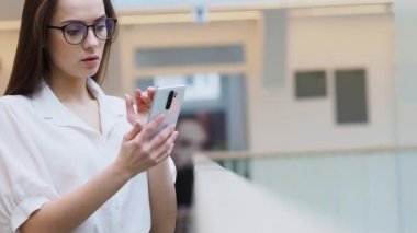 Şık iş kıyafetleri içinde genç bir kadın akıllı telefon kullanıyor.,