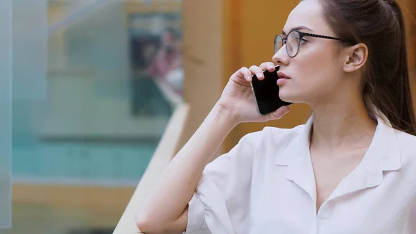 Jovem empresária usa um smartphone. Uma menina de camisa branca e óculos faz um telefonema . — Fotografia de Stock