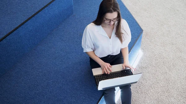 Joven estudiante utiliza un ordenador portátil. Una joven morena se sienta y escribe en un teclado , — Foto de Stock