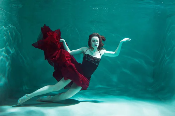 Schöne Mädchen in einem roten Kleid schwimmt unter Wasser. Erstaunliche Unterwasserwelt — Stockfoto