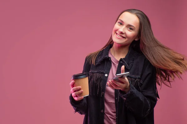 Joven estudiante con una taza de café de cartón y un teléfono inteligente en sus manos . — Foto de Stock