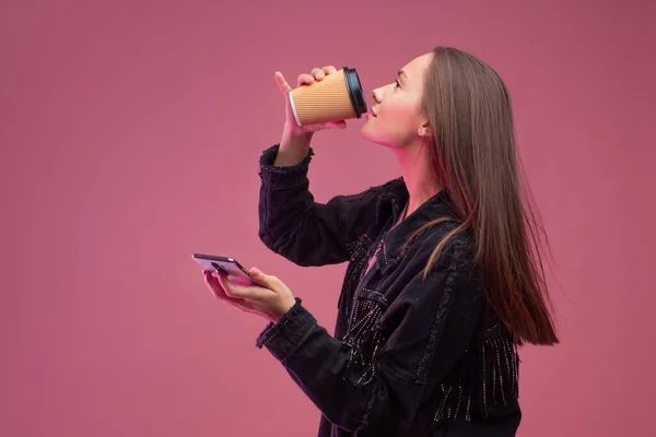 Giovane studentessa con una tazza di caffè in cartone e uno smartphone in mano . — Foto Stock