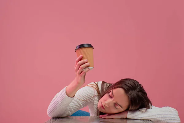 Schläfriges Studentenmädchen schläft und zieht ihre Hand mit einer Tasse Kaffee nach oben und bittet um eine zweite Tasse Kaffee, — Stockfoto