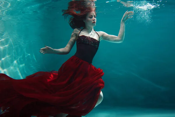 Mooi meisje in een rode jurk zwemt onder water. verbazingwekkende onderwater — Stockfoto