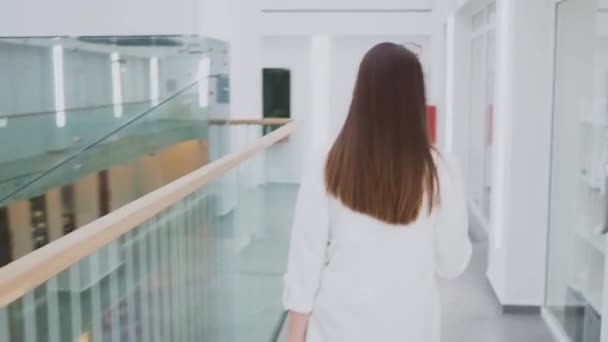 Jonge vrouw in stijlvolle zakelijke kleding loopt door een business center — Stockvideo