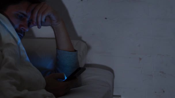 Jovem na cama à noite usa um smartphone. Insónia e dependência digital, a menina na cama — Vídeo de Stock