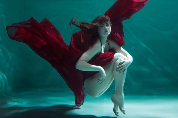 Krásná dívka v červených šatech plave pod vodou. úžasný podvodní — Stock fotografie