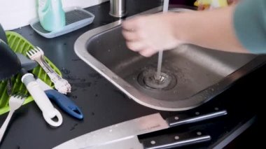 Elle bulaşık yıkayan, eldivensiz genç bir kadın bıçakları yıkıyor.