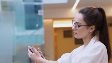 Genç iş kadını akıllı telefon kullanıyor. Beyaz gömlekli ve gözlüklü bir kız telefon eder..