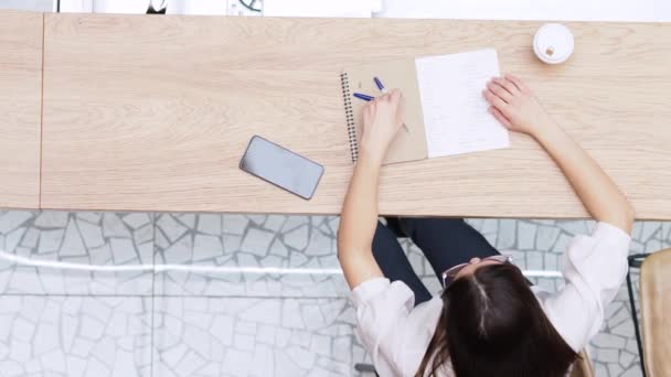 Estudante menina repete o material antes da lição. Jovem morena sentada à mesa com caderno — Vídeo de Stock