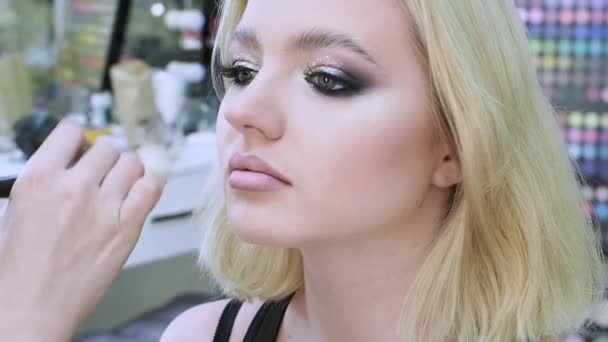Joven mujer rubia en una sesión con un artista de maquillaje, artista de maquillaje aplica polvo , — Vídeos de Stock