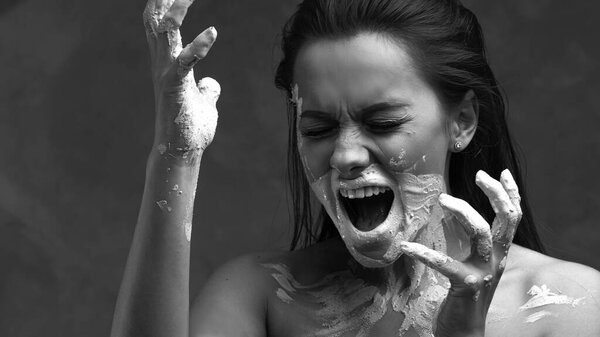 Scream, psychology. Portrait of a young beautiful woman with paint or clay on her face