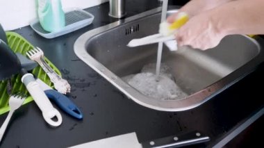 Elle bulaşık yıkayan, eldivensiz genç bir kadın bıçakları yıkıyor.